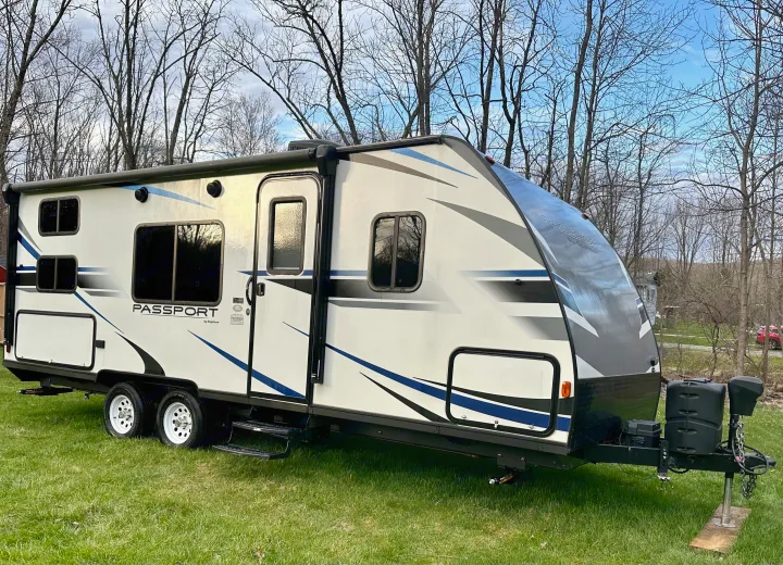 A clean white and blue Keystone Passport travel trailer RV for potential rv rental, parked on grass with bare trees in background.. Keystone RV Passport Express 2019