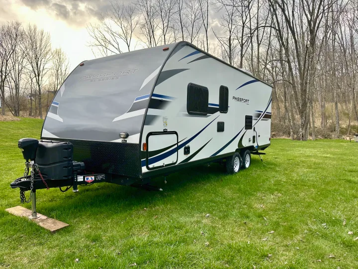 RV rental: A sleek Passport travel trailer, grey and white with blue accents, parked on vibrant green grass, ready for adventure.. Keystone RV Passport Express 2019