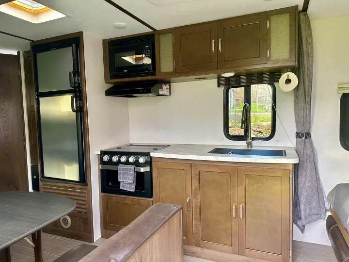This clean RV rental interior features a well-equipped kitchen with a fridge, microwave, stove, sink, and a dinette area.. Keystone RV Passport Express 2019