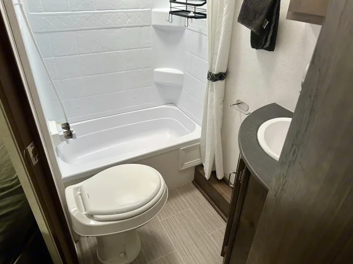 Compact RV rental bathroom: bright shower/tub, clean toilet, vanity with sink. Ideal for travel comfort.. Keystone RV Passport Express 2019