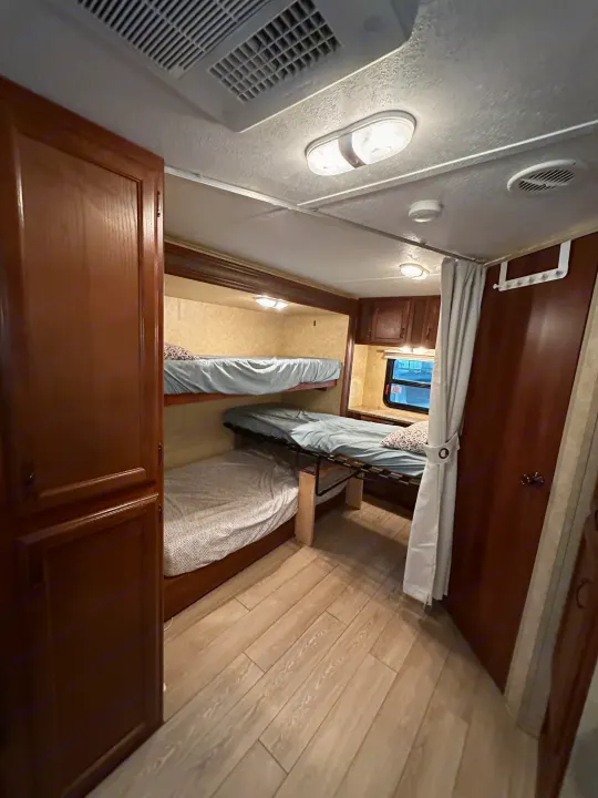 RV rental interior featuring comfortable bunk beds, light wood flooring, and overhead lighting. Ideal for family travel accommodations.. Forest River Tracer Executive 2010