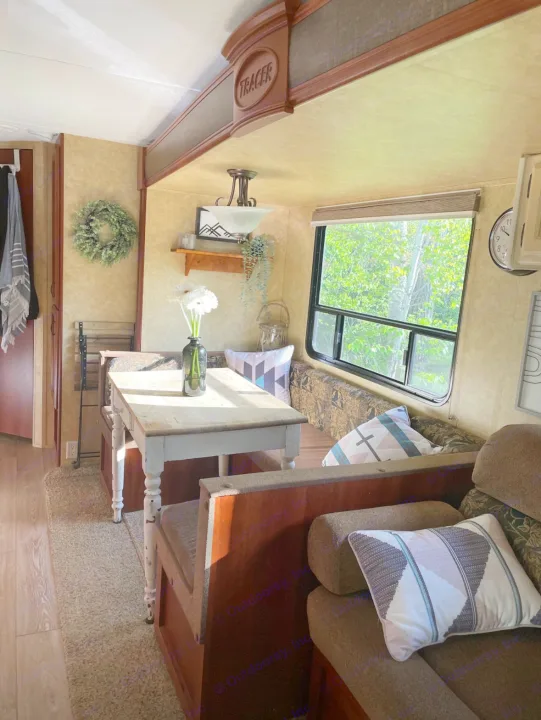 Cozy RV rental interior with a bright dinette, patterned cushions, and a window view of lush trees, ready for travel.. Forest River Tracer Executive 2010