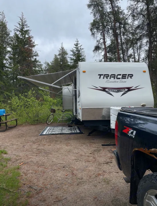 Tracer RV rental at a wooded campsite, with awning extended, picnic table, bicycle, and truck. Ready for camping.. Forest River Tracer Executive 2010