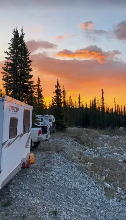 Stunning sunset lights up an RV rental, truck campers, and tall pines in a serene, rocky wilderness campsite.. Forest River Tracer Executive 2010