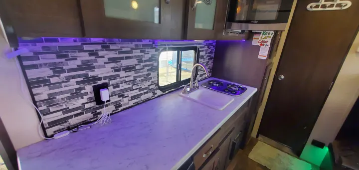 Explore this modern RV rental kitchen. Features a sink, stove, microwave, and cool purple LED lighting under cabinets.. Forest River Salem FSX 2019