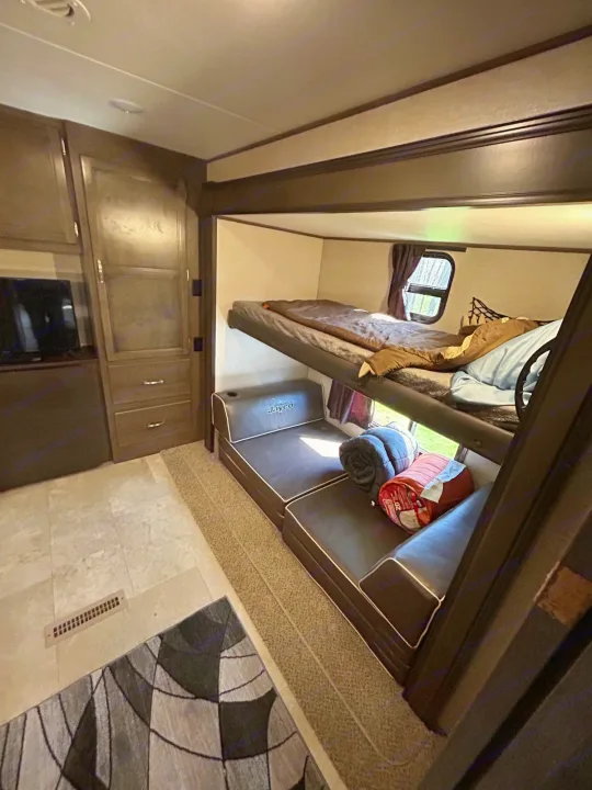 View inside an RV rental, featuring bunk beds, a lower sofa/bed, and cabinet storage. A practical camper interior for travel.. Jayco Jay Flight 2020