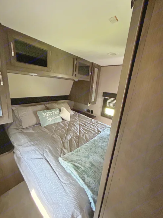Inside an RV rental, a compact bedroom features a bed with gray bedding, overhead storage, and a small window for a comfortable travel stay.. Jayco Jay Flight 2020