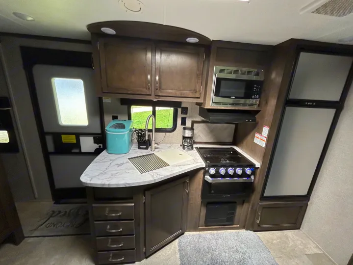 RV rental interior: a compact kitchen with dark cabinets, marble-look counter, sink, stove, microwave, and fridge.. Jayco Jay Flight 2020