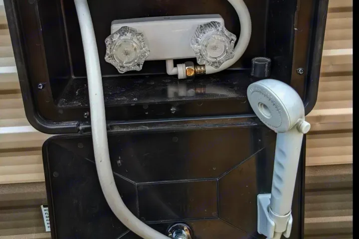 RV rental outdoor shower setup: clear hot/cold knobs, white hose, and sprayer head inside a black compartment. Great for campsite use.. Forest River Cherokee Grey Wolf 2014