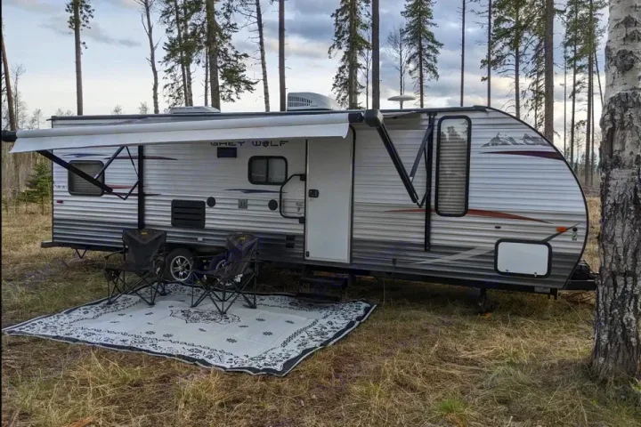 RV rental: A Grey Wolf travel trailer with awning, rug, & chairs set up in a peaceful forest campsite.. Forest River Cherokee Grey Wolf 2014