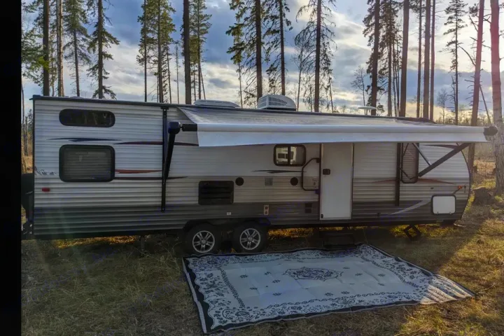 RV rental travel trailer set up in a sunny forest clearing, awning extended over a patterned outdoor mat.. Forest River Cherokee Grey Wolf 2014