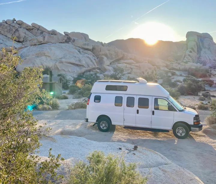 A white RV rental is parked on light-colored ground amidst large desert rocks and sparse brush during sunrise.. Chevrolet Express EXT 3500 2008