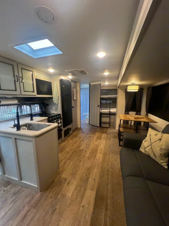 Spacious modern RV rental interior featuring a full kitchen, dining area, comfy sofa, and bunk beds.. Forest River Vibe 2021