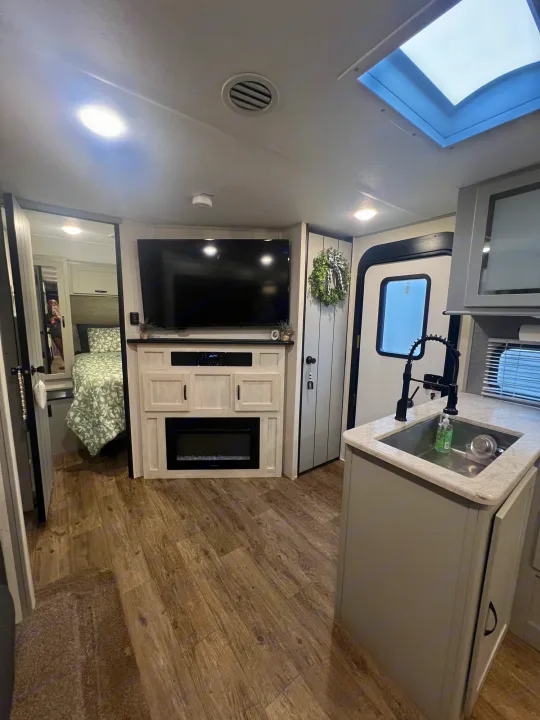 Bright RV rental interior: living area with TV/fireplace, compact kitchen, and inviting bedroom beyond.. Forest River Vibe 2021