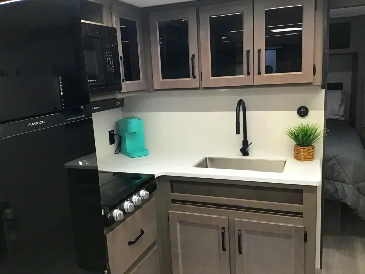 Compact, stylish RV rental kitchen with black fridge, microwave, gas range, sink, and light wood cabinets.. Grand Design Transcend Xplor 2024