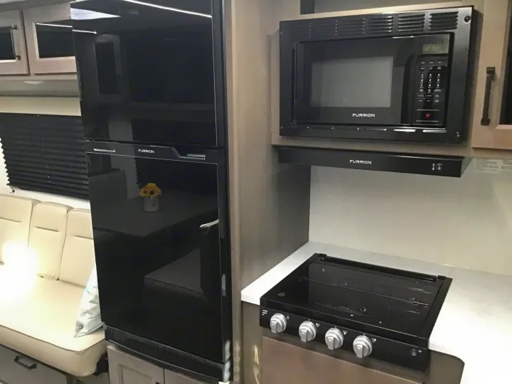 Spacious rv rental kitchen with black Furrion appliances: refrigerator, microwave, range hood, and four-burner stovetop.. Grand Design Transcend Xplor 2024