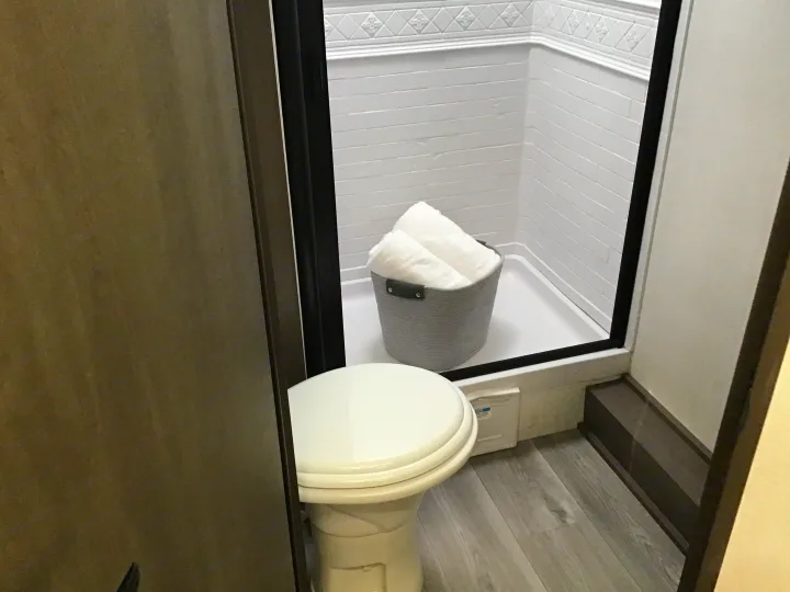 Inside an RV rental: a compact bathroom with a white toilet and tiled shower, complete with fresh towels.. Grand Design Transcend Xplor 2024