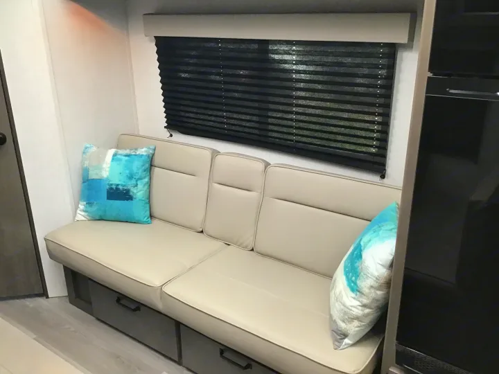 Cozy RV rental interior featuring comfortable bench seating with storage drawers, decorative pillows, and a window with black blinds.. Grand Design Transcend Xplor 2024