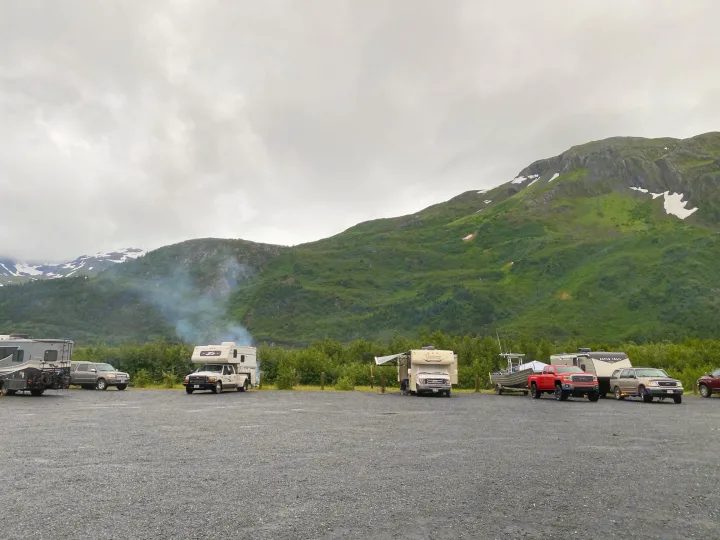 RV rentals and campers fill a gravel lot against a backdrop of green, snow-capped mountains under an overcast sky.. Forest River Coachmen Freelander 2015