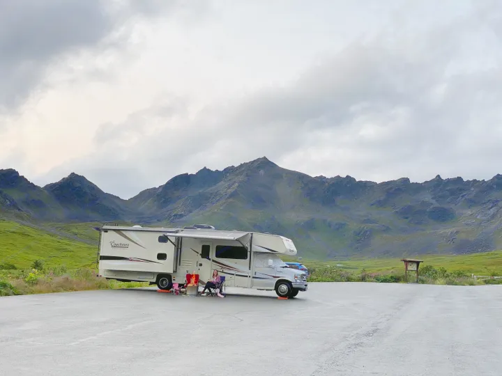 Scenic RV rental trip: A motorhome parked in a mountain valley, with a woman enjoying a campfire under a cloudy sky.. Forest River Coachmen Freelander 2015