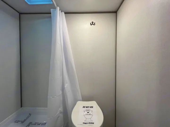 Inside an RV rental bathroom: a compact shower with white curtain, a vent above, and a toilet with a 'Do Not Use' sign.. Coleman Lantern LT 17 B 2024