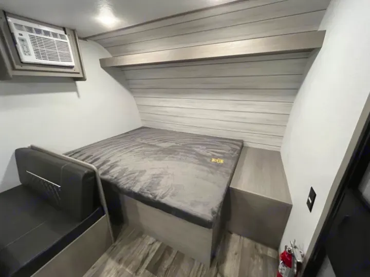This RV rental interior shows a cozy bed, AC, black bench, and wood-paneled walls, ready for camping.. Coleman Lantern LT 17 B 2024