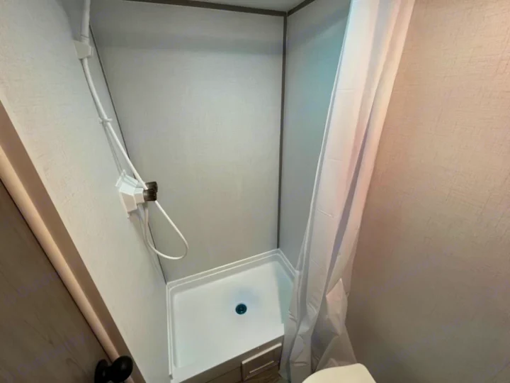 RV rental's compact bathroom shower stall. White walls, shower pan, and curtain are visible. Functional and space-saving.. Coleman Lantern LT 17 B 2024