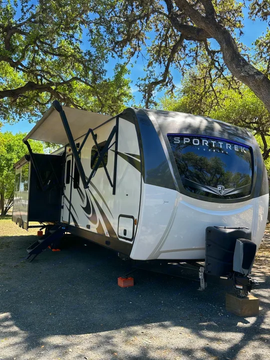 SportTrek Touring RV rental, fully set up with awning extended, parked at a peaceful, tree-shaded campsite.. Venture STT343VIB 2022