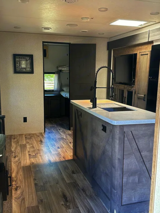 RV rental interior features a kitchen island with black faucet, wood-look floor, and a rear bunk room. Bright & ready for adventure.. Venture STT343VIB 2022