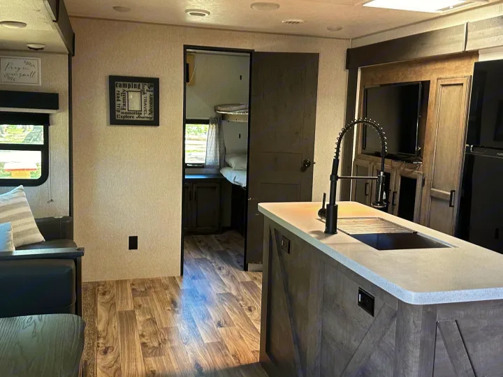 Inside a comfy RV rental: full kitchen island, living space, and bunk beds for family travel fun.. Venture STT343VIB 2022