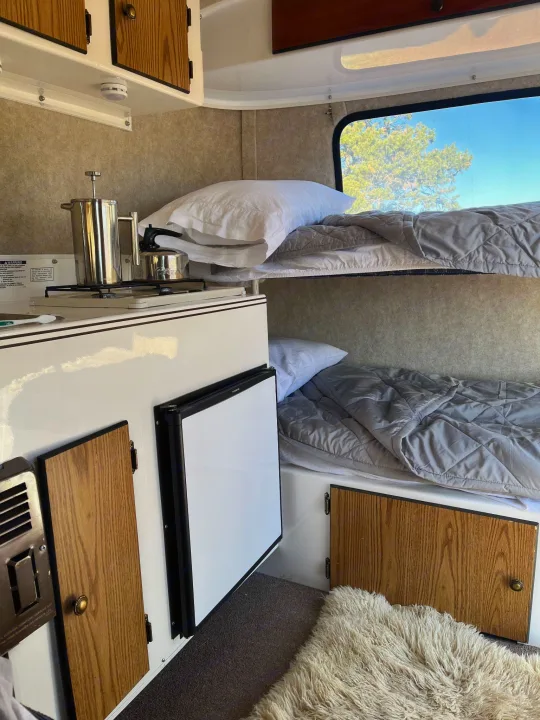 Compact RV rental interior featuring bunk beds, a small kitchen, and fridge for cozy adventures.. Scamp Scamp Trailer 2004