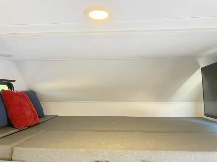Relaxing RV rental interior: grey bed, red and blue pillows, TV, and ceiling light. Ideal for a comfortable journey.. Forester LE 2024