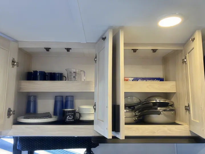 Well-organized kitchen storage in an RV rental, featuring dishes, mugs, pots, and pans in light wood cabinets.. Forester LE 2024
