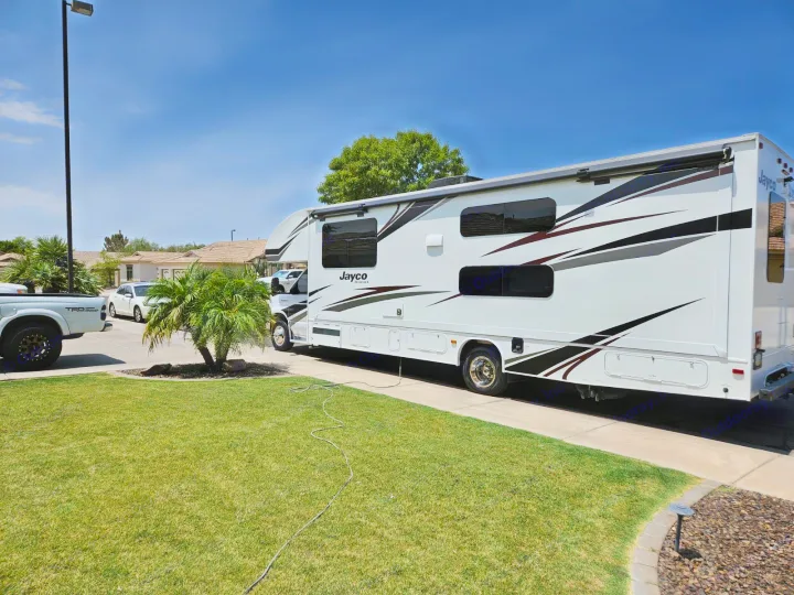 White Jayco rv rental parked in a sunny residential driveway with a green lawn, palm tree, and clear blue sky.. Jayco Redhawk 2020