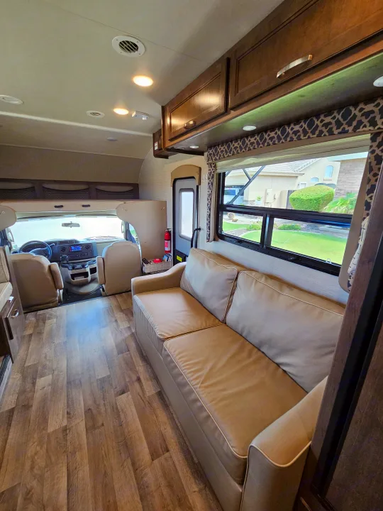 Spacious RV rental living area with a beige sofa, wood-look floor, and driver's cab visible. Ready for comfortable travel adventures!. Jayco Redhawk 2020