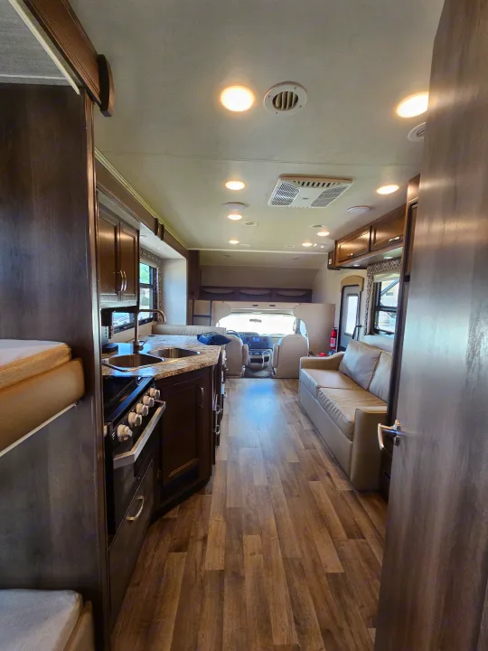 Bright, wood-paneled RV rental interior: kitchen, living area w/couch, driver's cab. Ready for travel.. Jayco Redhawk 2020