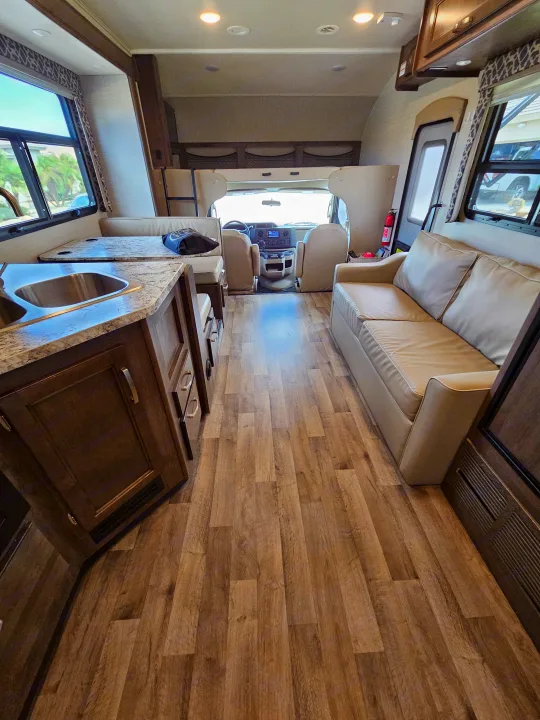 Spacious rv rental interior showing kitchen, dinette, sofa, and cockpit, with wood-look flooring throughout.. Jayco Redhawk 2020