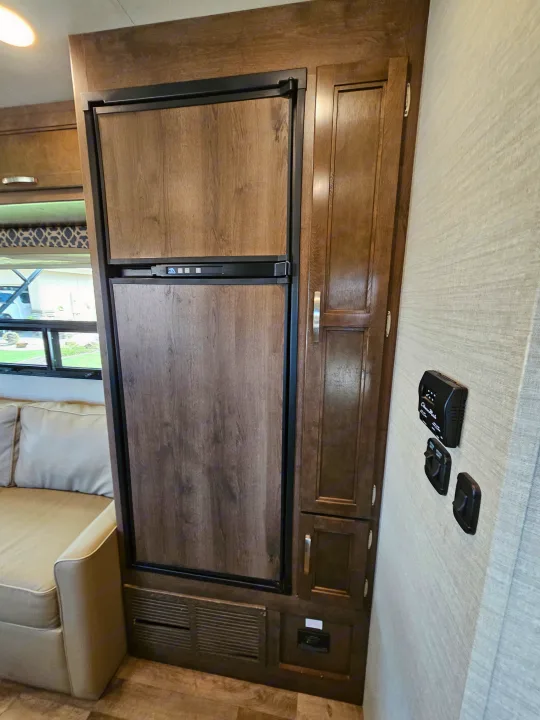 RV rental interior features a wood-paneled refrigerator, cabinetry, climate controls, and part of a couch.. Jayco Redhawk 2020