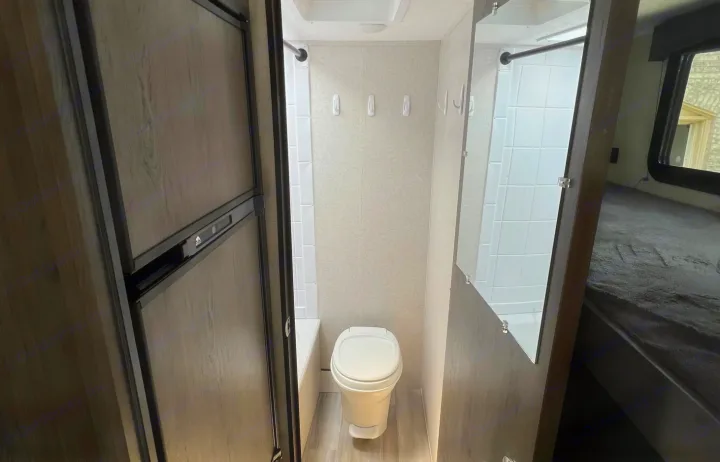Compact RV rental interior featuring a refrigerator, a bathroom with toilet and hooks, and a shower/bunk area on the right.. Clipper Ultra Lite 2022