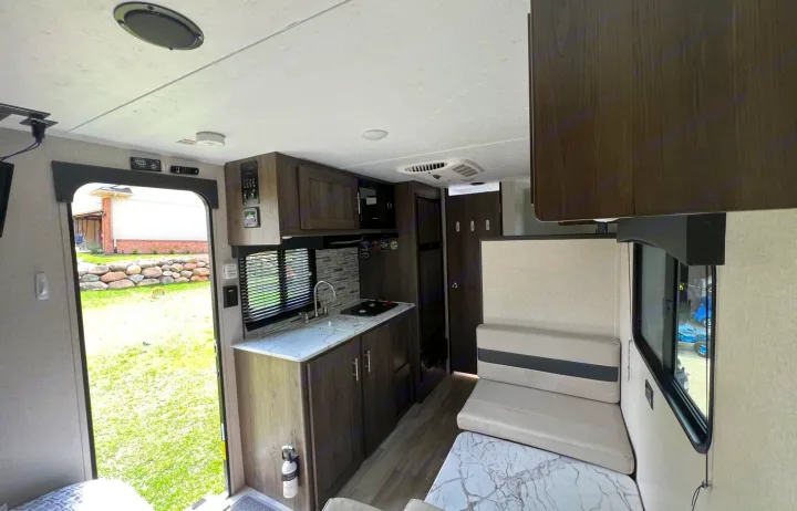 View inside an RV rental showing a compact kitchen with sink & stovetop, dinette, and open door to a grassy yard.. Clipper Ultra Lite 2022