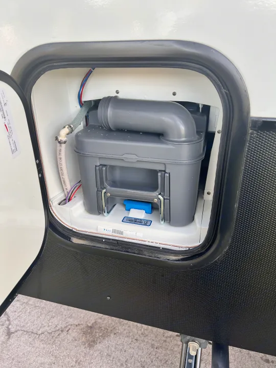An open exterior compartment on an RV rental reveals its removable waste cassette tank for sanitary maintenance.. Winnebago Hike 100 2023