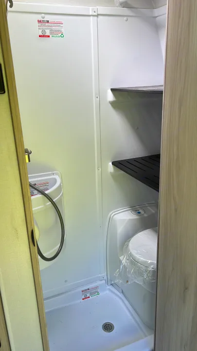 Compact RV rental wet bath with toilet, sink, shower, and shelving.. Winnebago Hike 100 2023