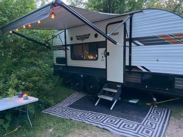 Cozy rv rental set up in a wooded campsite, featuring an extended awning with lights, outdoor rug, and table for relaxation.. Forest River Wildwood X-Lite 2020