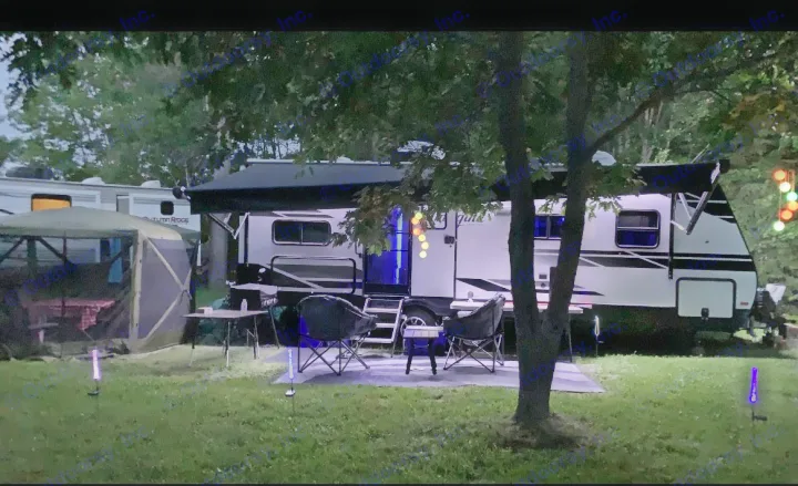 Illuminated campsite with an RV rental, set up for a relaxing evening. Includes a screened tent, chairs, and ambient lighting.. Grand Design imagine 2020