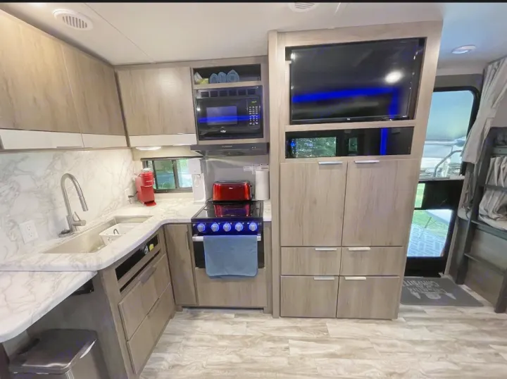 Spacious RV rental kitchen featuring a sink, stove, microwave, and TV. Ideal for travel trailer adventures.. Grand Design imagine 2020