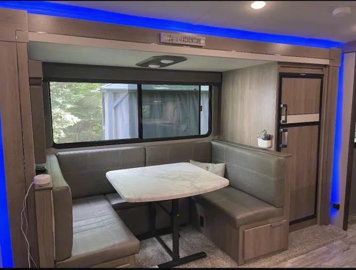 Modern RV rental dinette featuring comfortable booth seating, a table, window views, and stylish blue accent lighting.. Grand Design imagine 2020