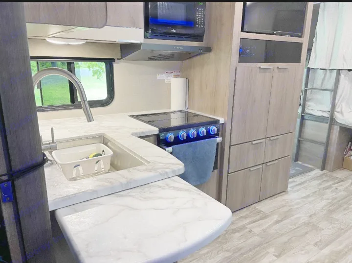 Modern RV rental kitchen with sink, stove, microwave, and bunk beds, featuring sleek counters & wood flooring.. Grand Design imagine 2020