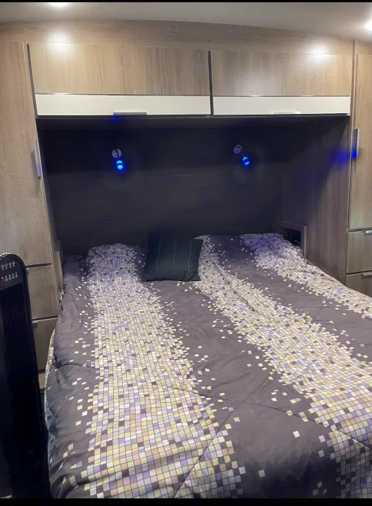 RV rental bedroom: bed with mosaic comforter, built-in storage, blue LED lights, and fan on the left.. Grand Design imagine 2020