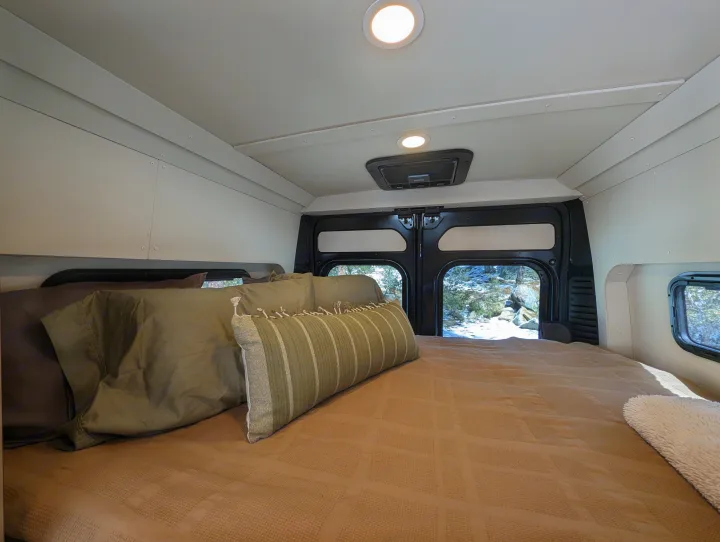 Cozy RV rental bed with a snowy view out the back doors. Ideal for winter getaways.. New Life Conversions Luxury Edition 2022