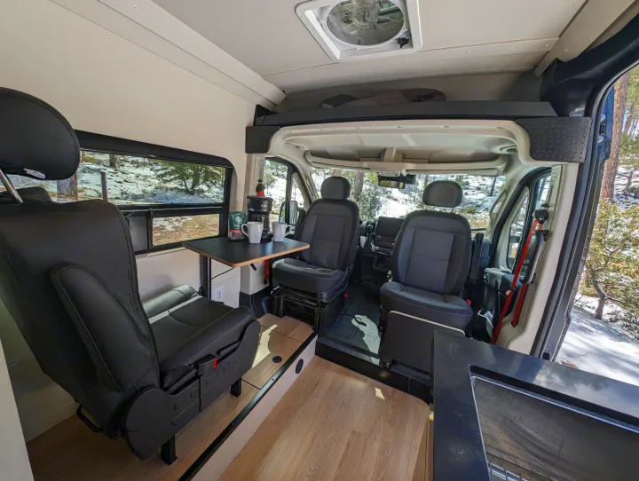 Bright and spacious RV rental interior: swiveling seats, dinette with coffee, overhead bunk, and scenic window views.. New Life Conversions Luxury Edition 2022